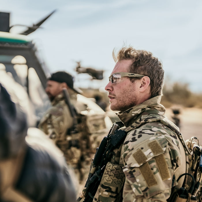 Militærperson med Wiley X briller og camouflage beklædning i ørkenmiljø, fokuseret udtryk